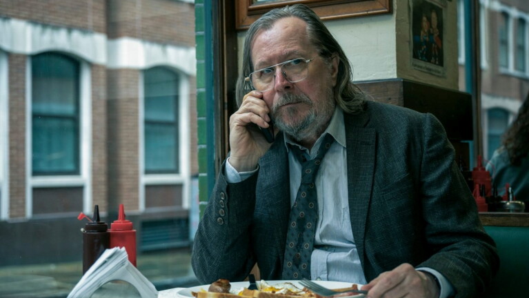 Gary Oldman on the phone whilst eating a cooked breakfast in a café