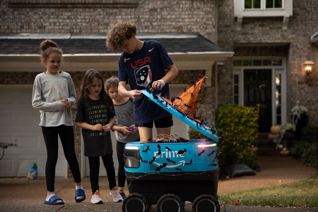 An image of kids looking at a Scout Robot in front of their house. The robot has Halloween decorations on it.