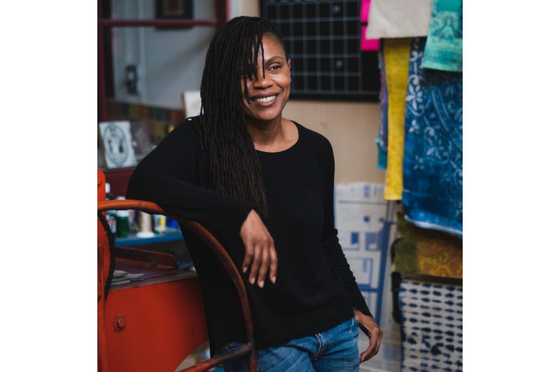 Jite Agbro smiles and looks off to the side in an art studio.