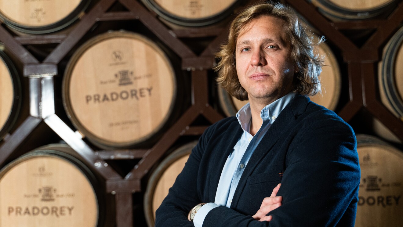 Javier Marco, responsable de E-commerce 0de Pradorey. En la bodega con tinajas de madera en segundo plano y en primer plano Javier Marco con los brazos cruzados mirando a cámara. Tiene media melena rubia, ojos azules y va vestido con una americana azul oscura y una camisa azul clarita.
