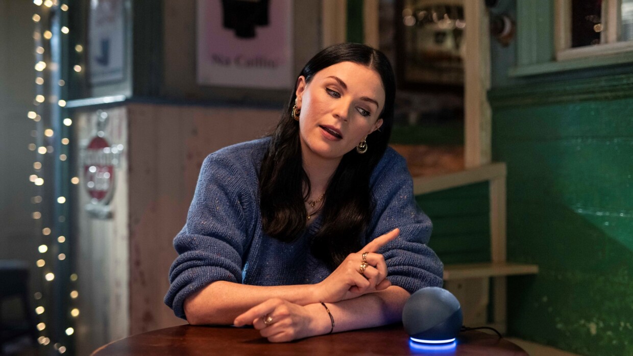 Aisling Bea sitting at a table talking to Alexa with an Amazon Echo Device