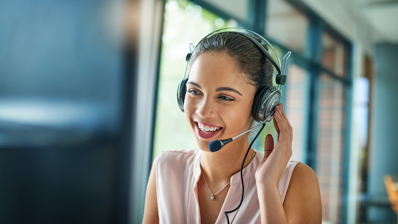 A woman on a headset works on a computer screen. 