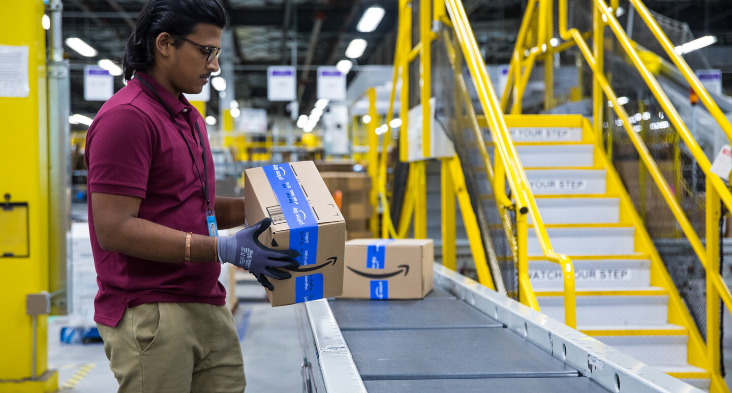A photo of a fulfilment center employee holding an Amazon delivery box