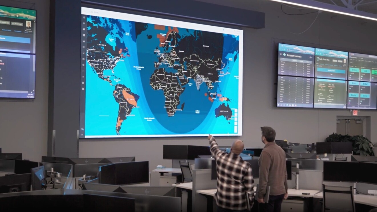 Two Amazon employees at operations center with interactive world map and data screens