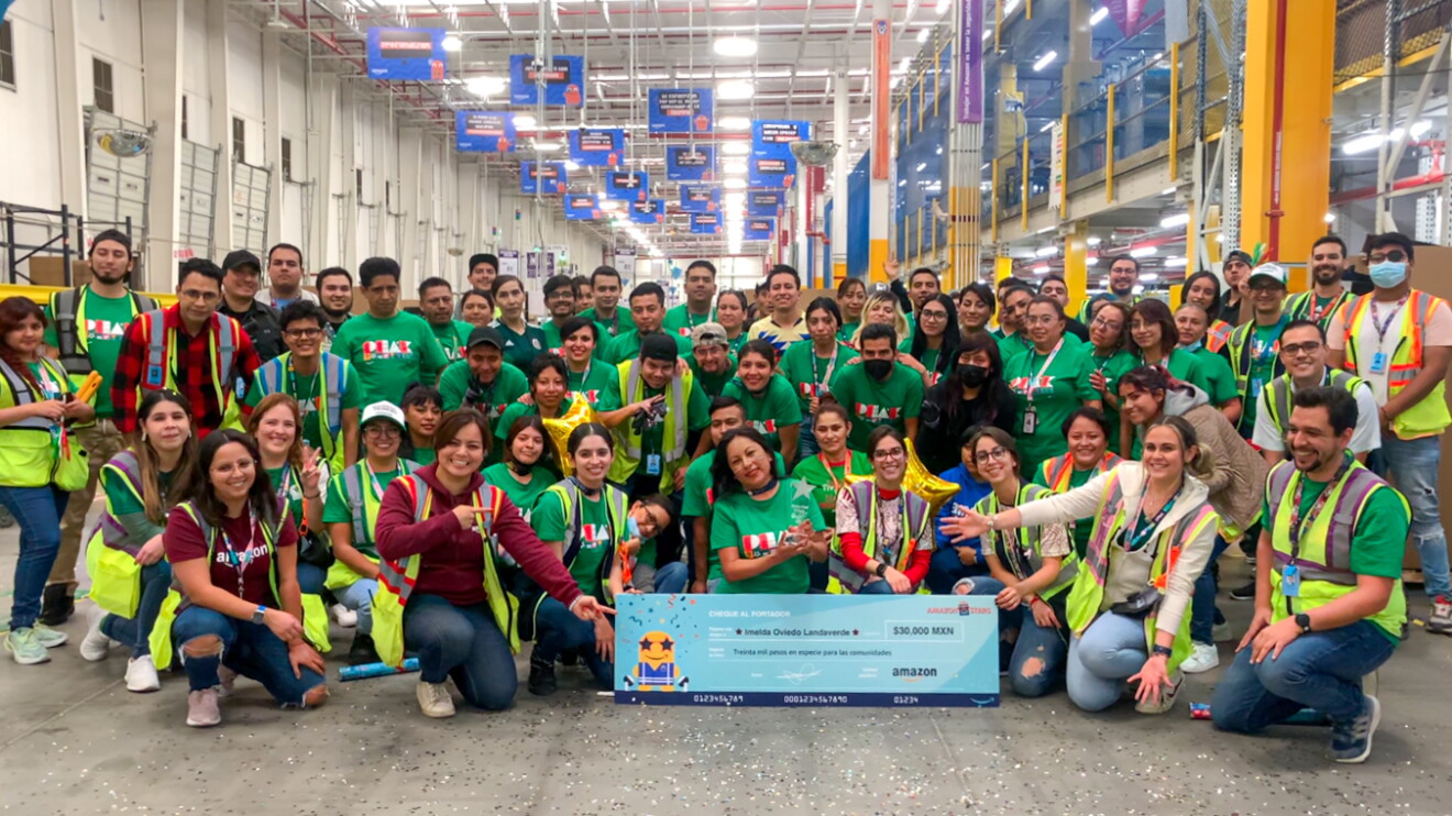En un centro logístico, más de 70 trabajadores de un centro logístico posant con un cheque de Amazon Stars.  