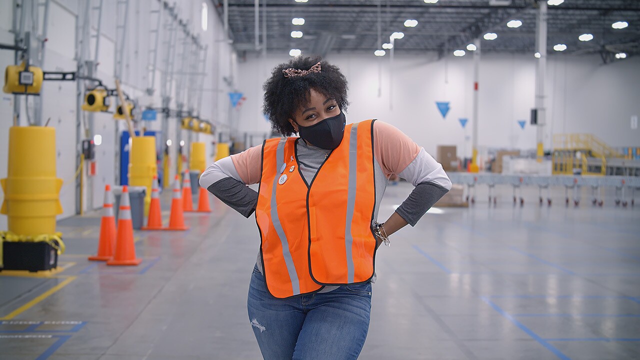 a Black woman who is an Amazon employee looks at the camera. She is wearing a face mask.