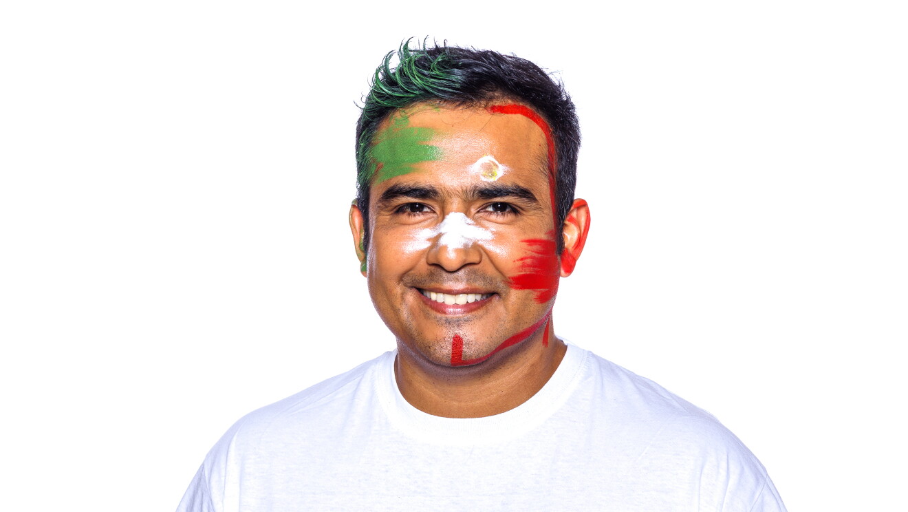 Para el Día de la diversida Amazon ha preparado una acción con asociados de diferentes países que llevan la bandera pitnada en su cara. En la foto, Ricardo con camiseta blanca, mirando sonriendo a cámara con la bandera de su país puntada en la cara. Tiene el pelo negro y corto. No lleva barba. 