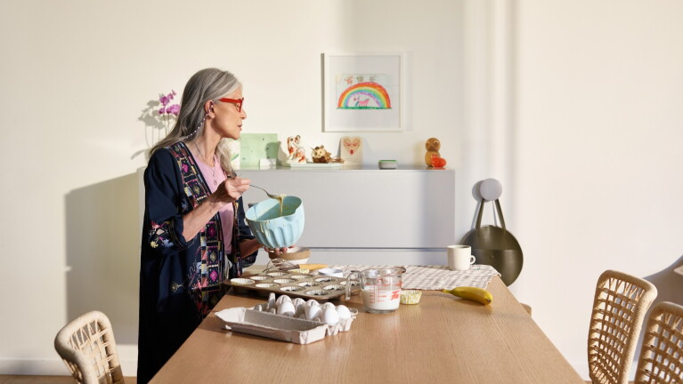 Older woman baking in bright kitchen with rainbow artwork