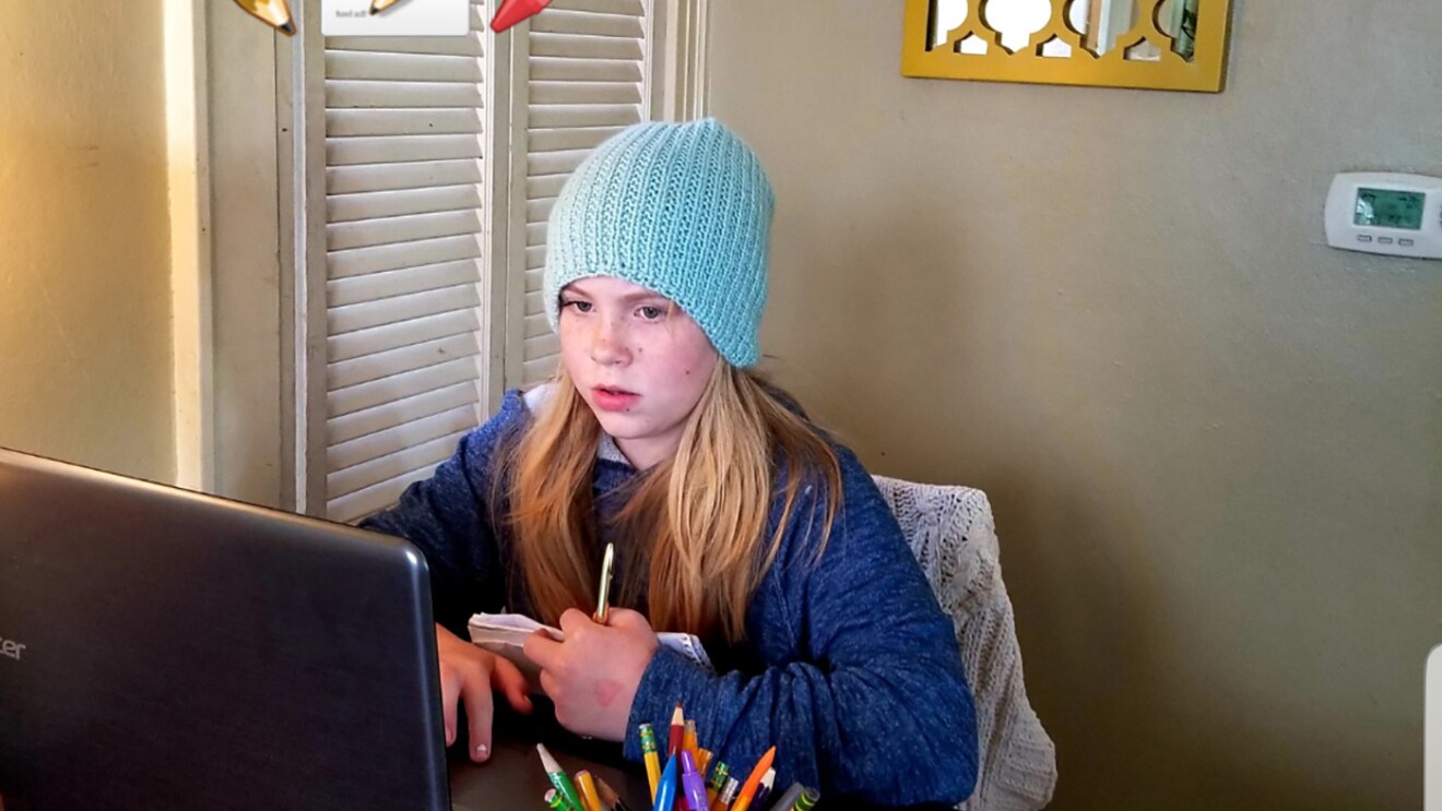 An elementary age student sits with their laptop computer in their home
