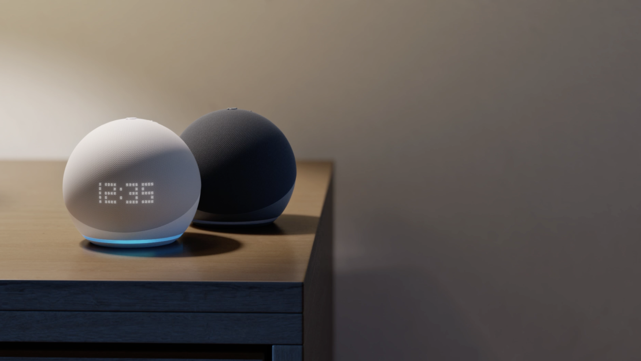 Due dispositivi Echo su un tavolo. Un dispositivo è grigio e ha il display con l'orologio acceso. L'altro è nero ed è in secondo piano. 