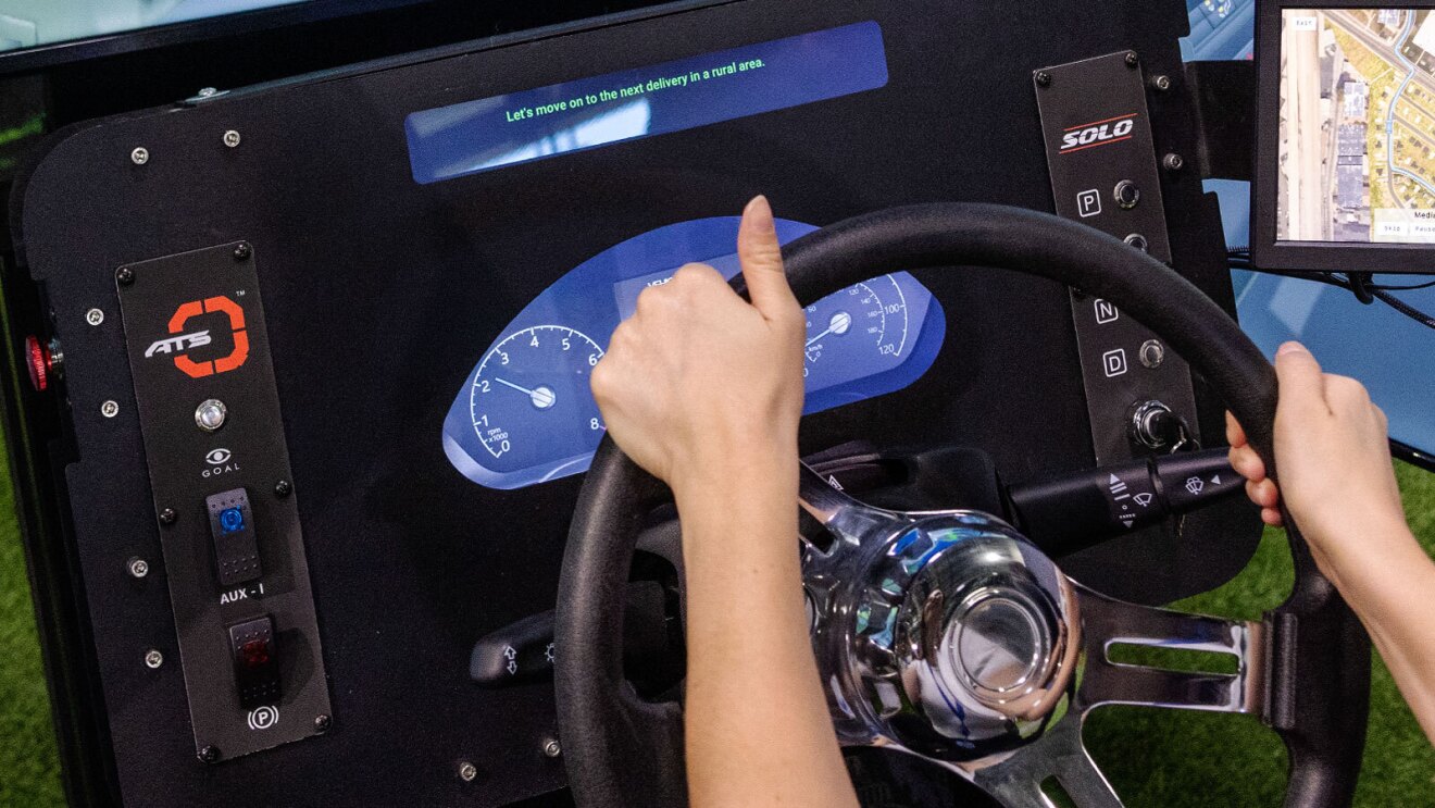 An image of the dashboard on a driver simulator for the Rivian delivery van. It shows a steering wheel, a speedometer, buttons for shifting gears, and various other controls.