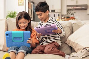 An image of two children using their Amazon tablets while sitting on the sofa. 