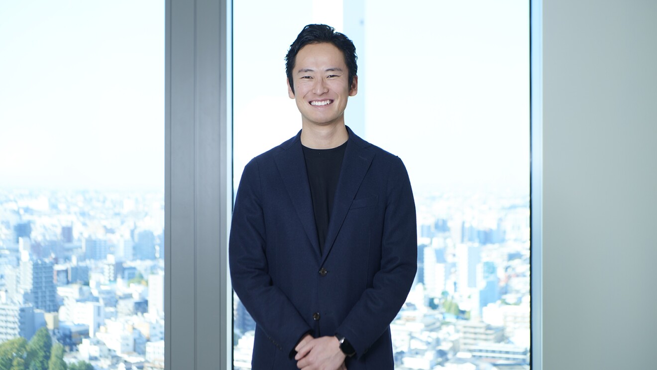 高層ビルの窓辺に立つ紺色のジャケットを着た男性