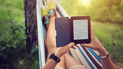 Donna legge un Kindle distesa su un'amaca in mezzo al verde.