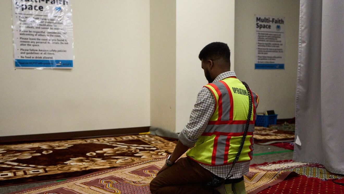 An image of Abdiaziz, an area manager working in an Amazon fulfillment center, kneeling on a rug in prayer.