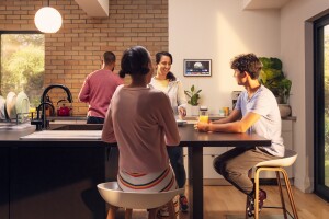 An image of four people interacting in a kitchen with an Echo Show 15 mounted to the wall in the background. 