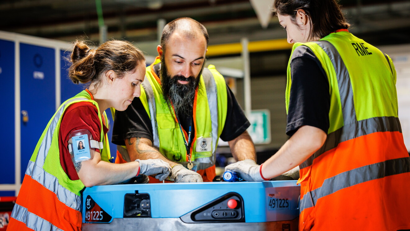 Tre trabajadores de un centro logístico de Amazon arreglando un robot. 