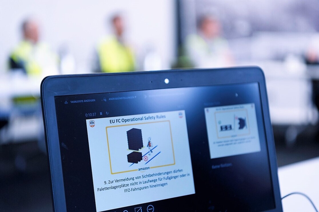 Auf einem aufgeklappten Laptop-Bildschirm ist zu lesen: "Zur Vermeidung von Sichtbehinderungen dürfen Palettenlagerplätze nicht in Laufwege für Fußgänger oder in FFZ-Fahrspuren hineinragen." Dazu sieht mal eine Illustrationen, die das richtige/falsche Abstellen darstellt.