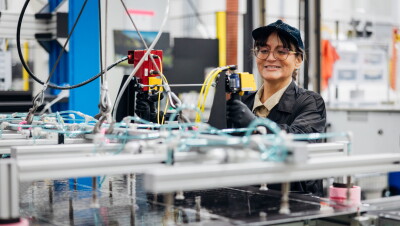 Female fulfillment center worker smiling while operating manufacturing equipment with robotic arms
