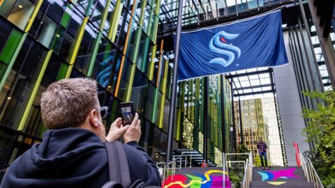 人拿着他的手机,拍照的西雅图巨妖国旗挂在西雅图市中心的两栋建筑之间。