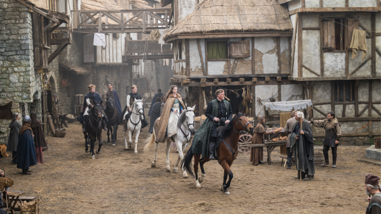 People on horseback riding through a medieval town while wearing period clothing