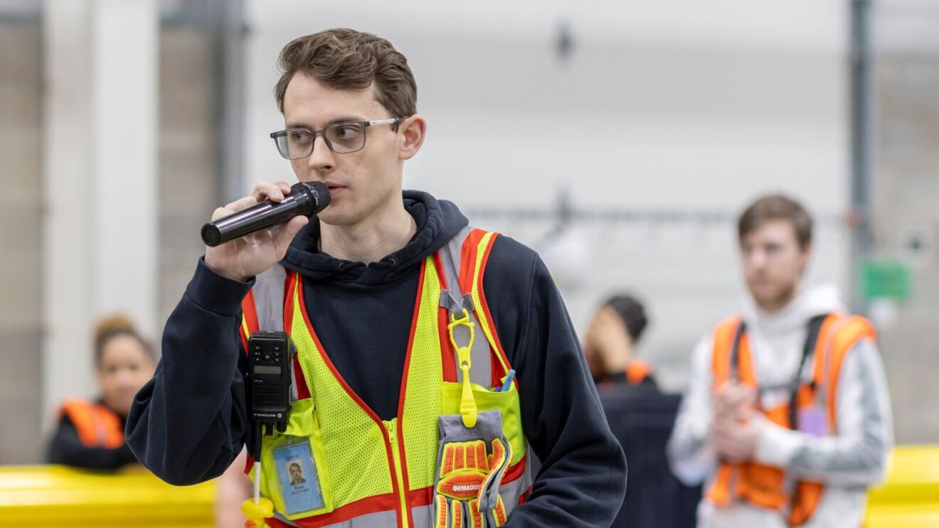 Worker in safety vest speaking into microphone.
