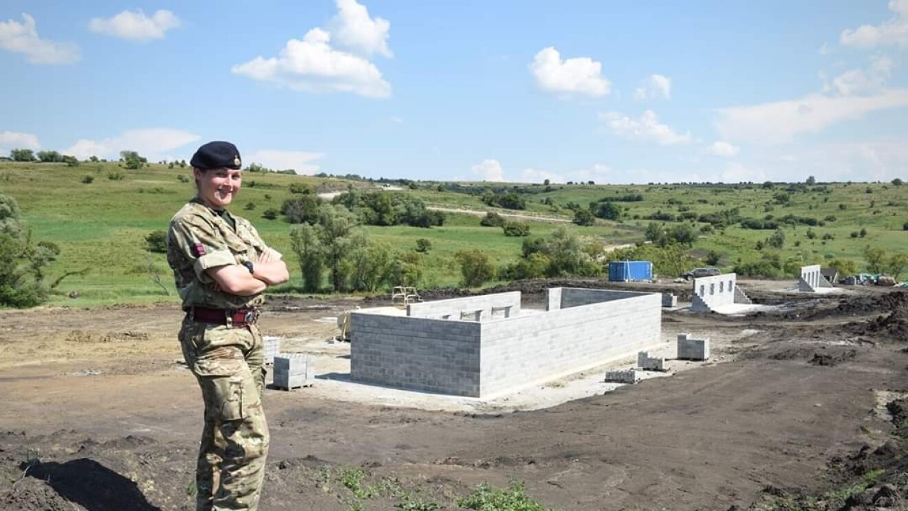 Reservist, Sophie Martin, standing cross-armed and dressed in her Army uniform with an outdoor military facility in the background.