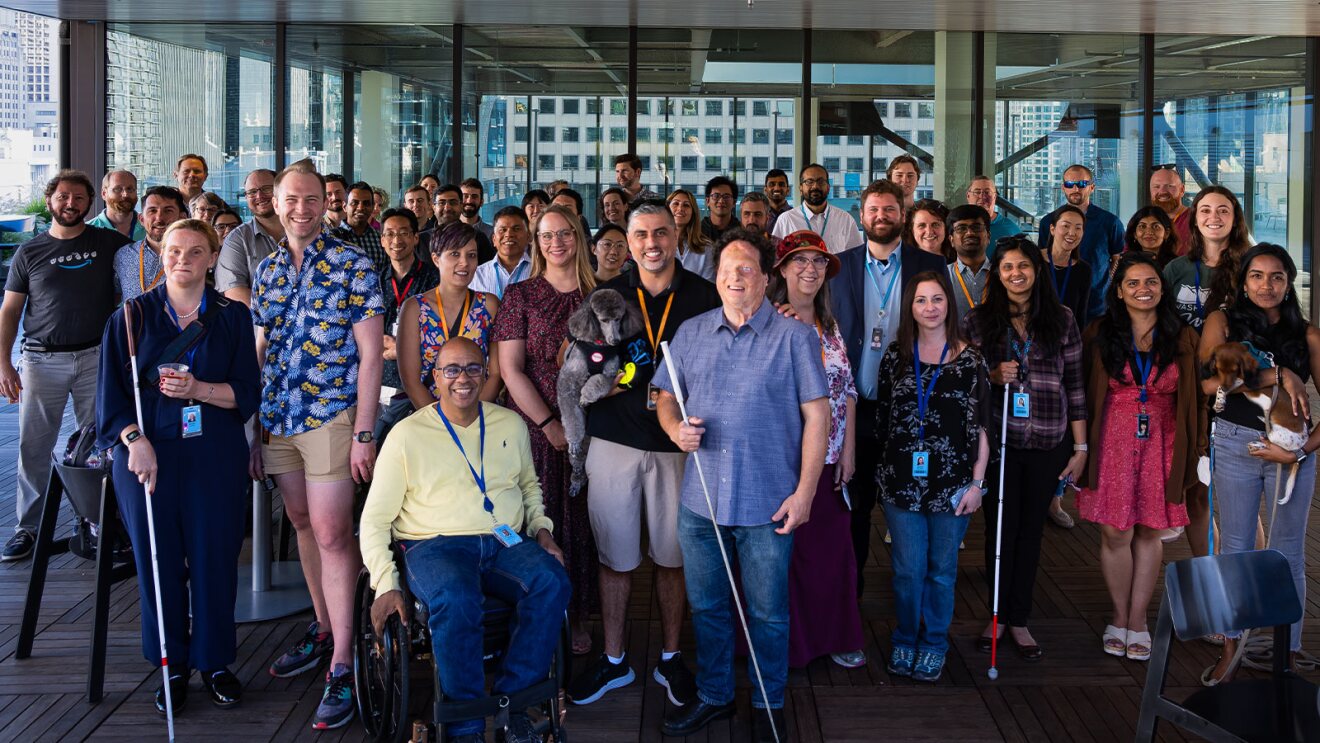Large team photo showcasing inclusivity with wheelchair user and guide dogs