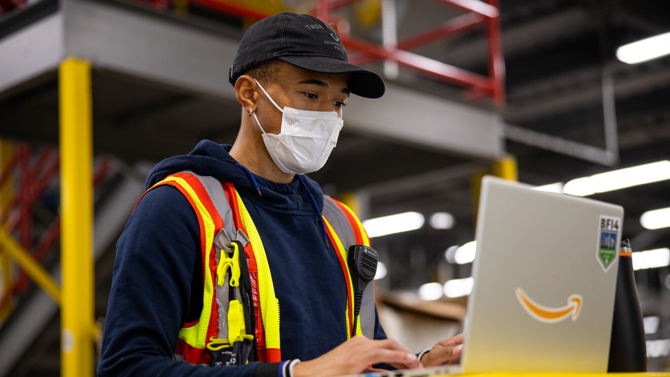 A man is wearing a mask while working on a laptop in one of Amazon's fulfillment centers.