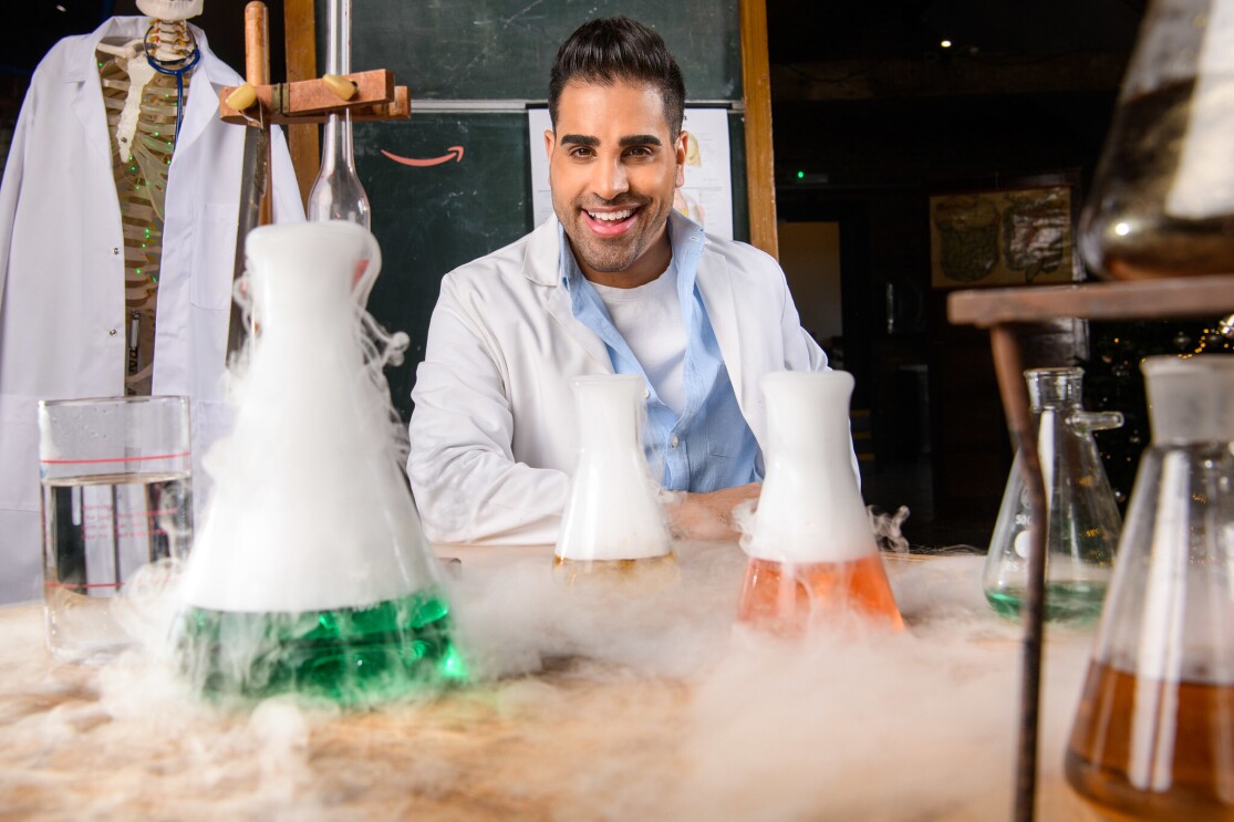 Dr. Ranj Magic Breakfast in front of a table filled with test tubes and science experiments.