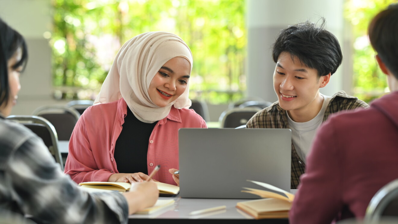 A diverse group of youths looking at the screen of a laptop.