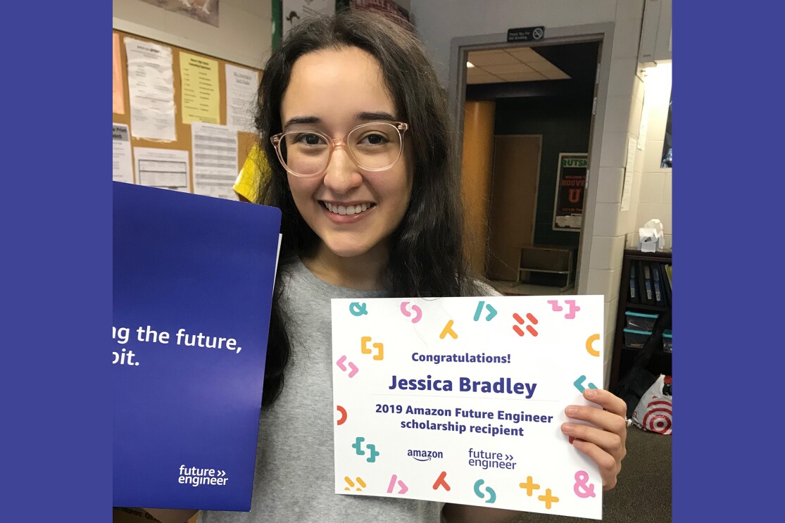 A young woman who is a high school senior smiles at the camera and shows her 2019 Amazon future engineer scholarship award announcement. 