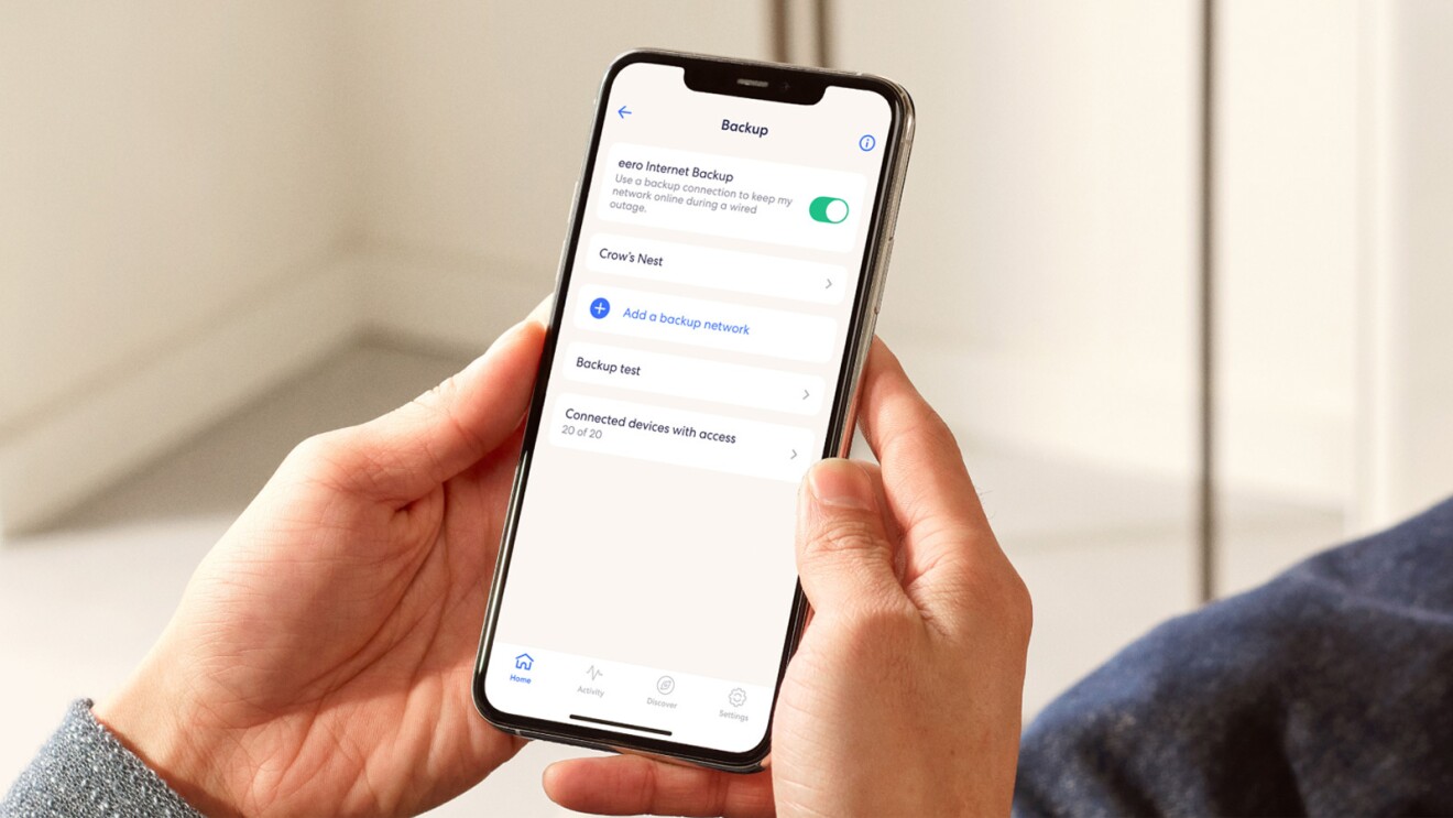 An image of two hands holding a phone that shows eero Internet Backup settings.