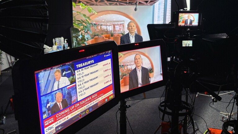 Primary monitors display an interview segment from what appears to be CNBC's Squawk Box, featuring Amazon CEO Andy Jassy in a dark blazer and white shirt.
