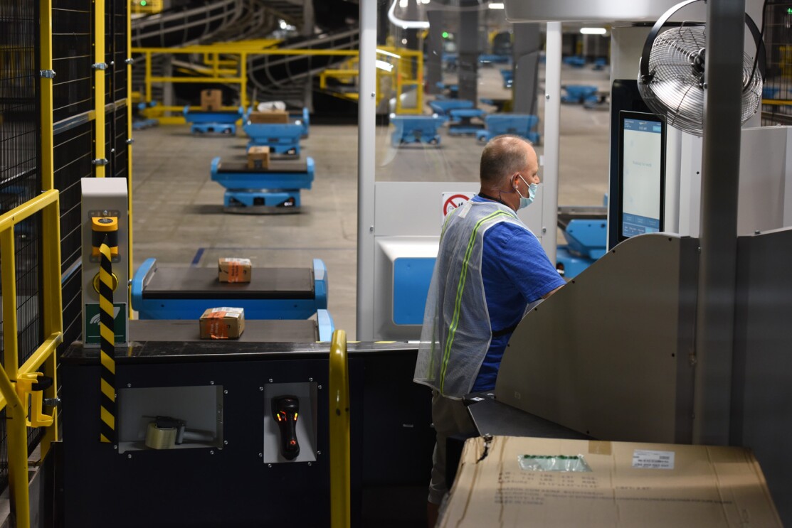 An image of small, blue robots with packages on them rolling through an Amazon sortation center.