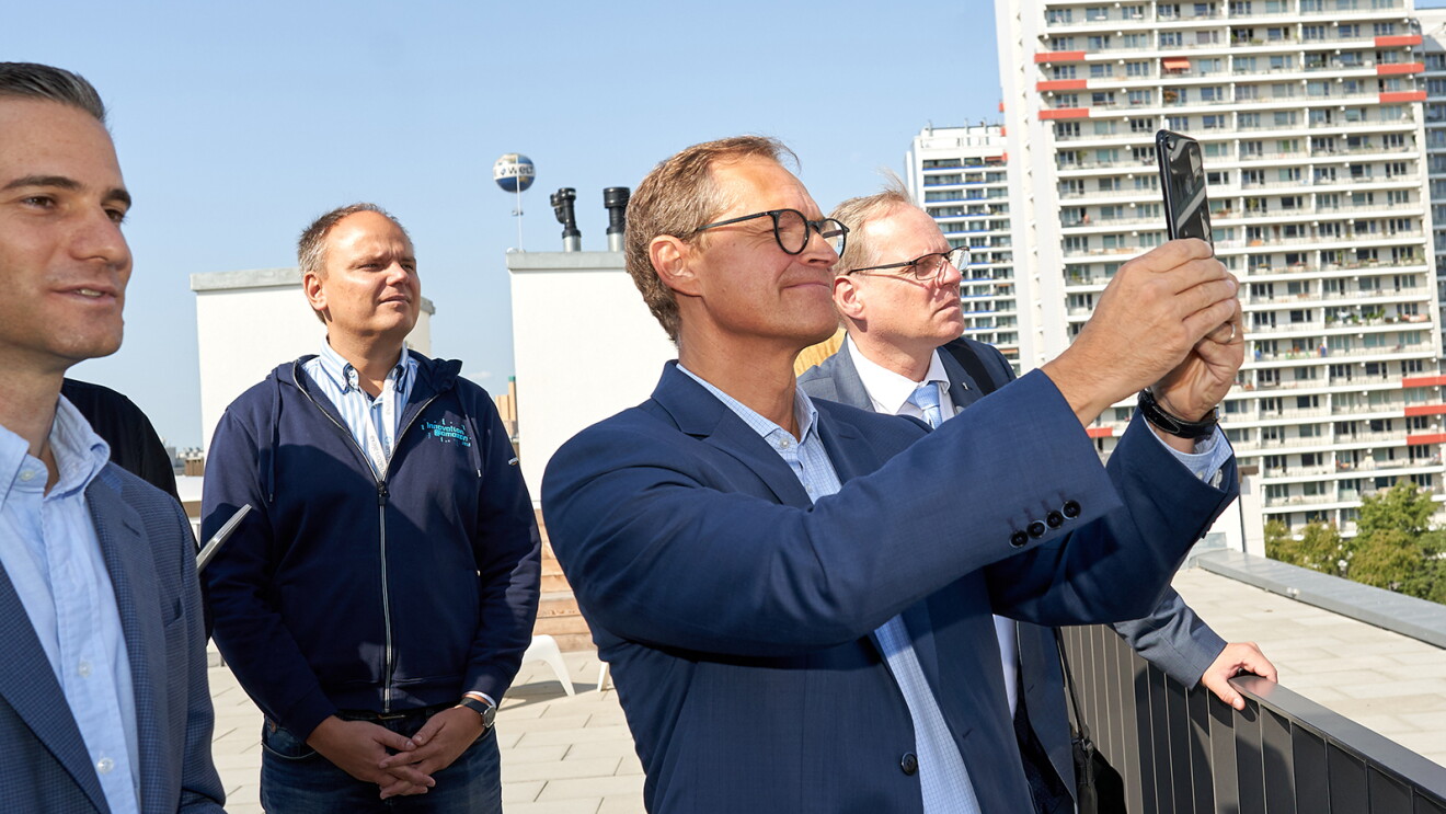 Der Bürgermeister von Berlin, Michael Müller, steht mir den Amazon Kollegen auf dem Dach den Amazon-Gebäudes. Sie genießen die Aussicht und machen Fotos der Skyline.