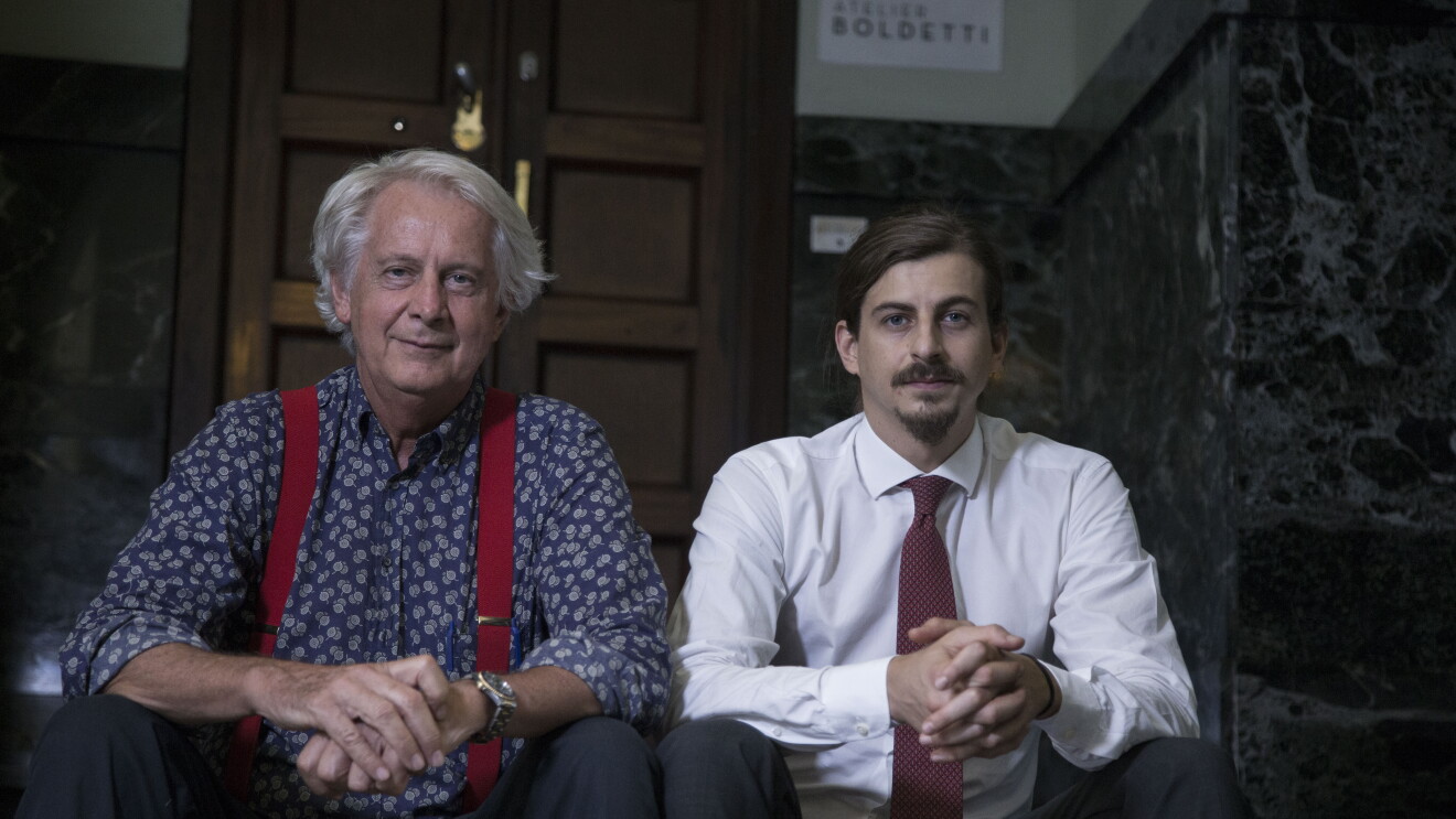 Due uomini sono seduti fianco a fianco su uno scalino all'ingresso di un palazzo. A sinistra Giorgio Boldetti, e accanto a lui Giulio Boldetti, 32 anni, entrambi proprietari dell’Atelier Boldetti di Torino. 