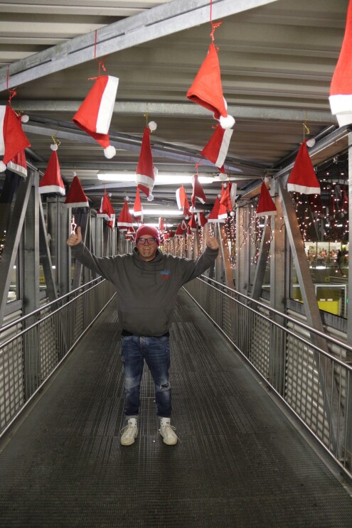 DJ Ötzi ist auf einem Gang zu sehen, über ihm hängen zahlreiche Weihnachtsmützen