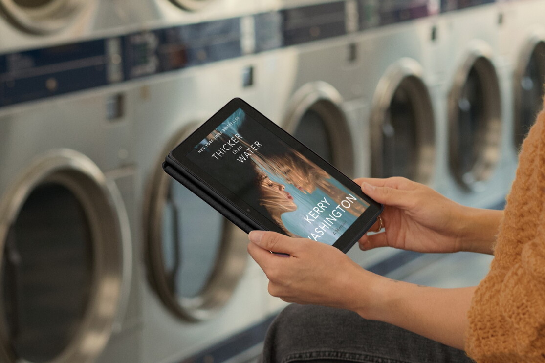 コインランドリーで黄色いセーターを着ている人は本の表紙が表示されているタブレットを持っている。