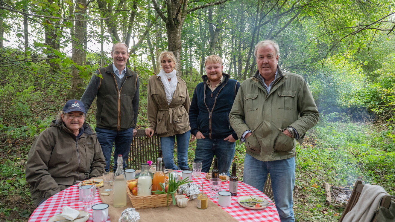 Five people posing for a picture, standing around a table with food and drinks on it