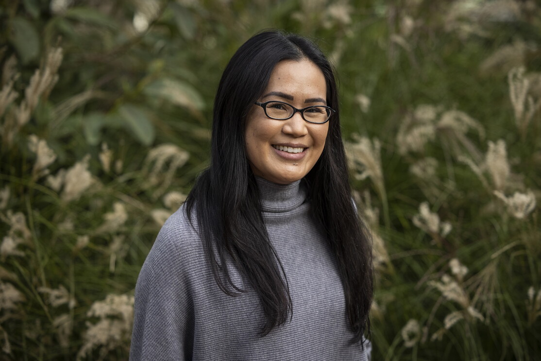 An image of a woman smiling for a professional photo in front of a green area outside.