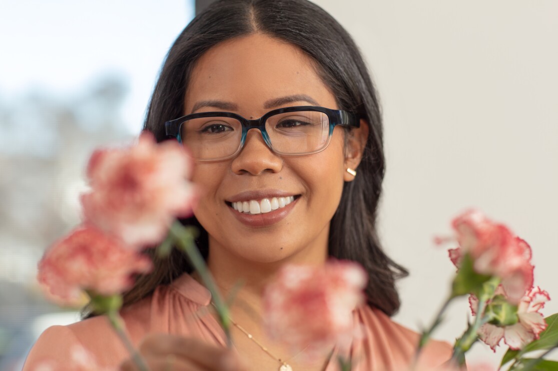 A woman wears Echo Frames in pacific blue and smiles as she looks at flowers.