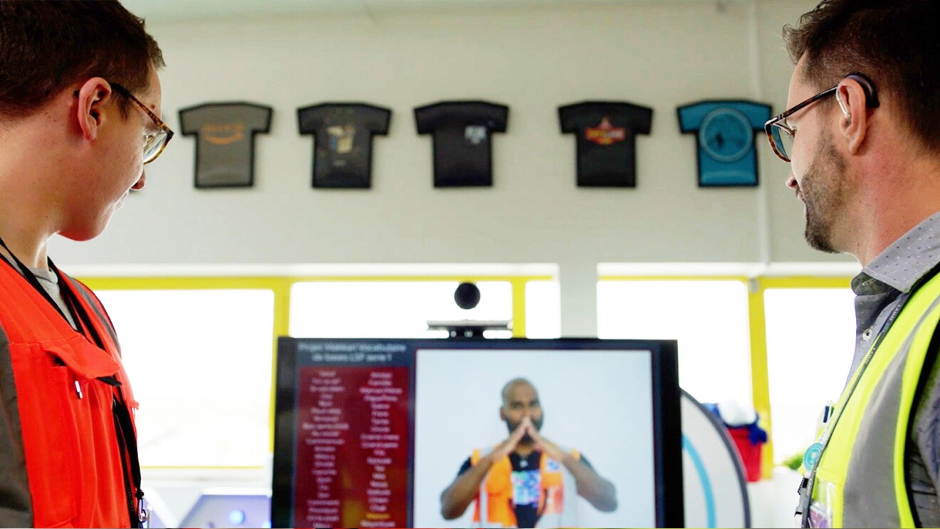 A photo of two employees at a video station within an operations center, reviewing a sign language tutorial.