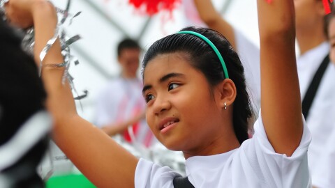 Girl with green headband in the crowd, cheering with pom poms