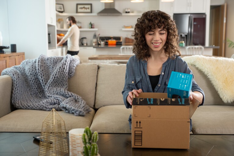 An Amazon customer smiles as they unbox a package on their couch.