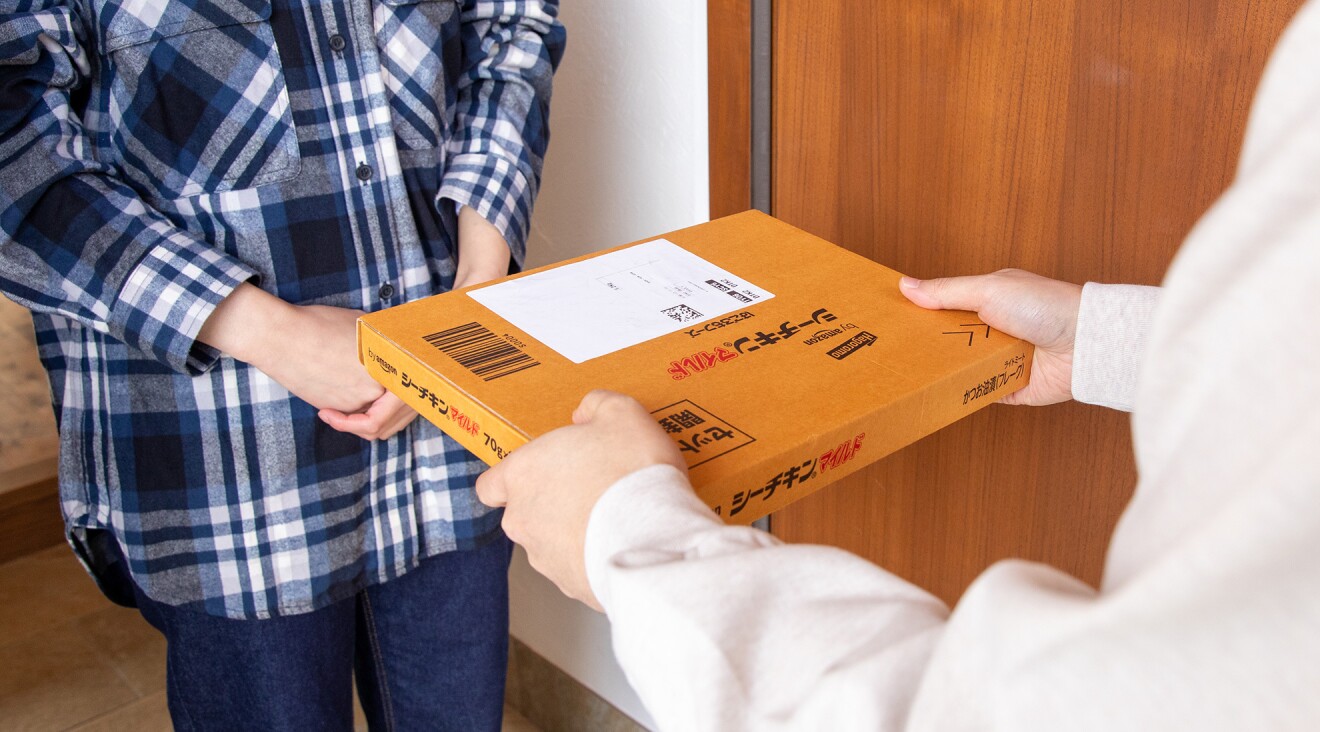 玄関で商品名が入った箱を手渡す配達員