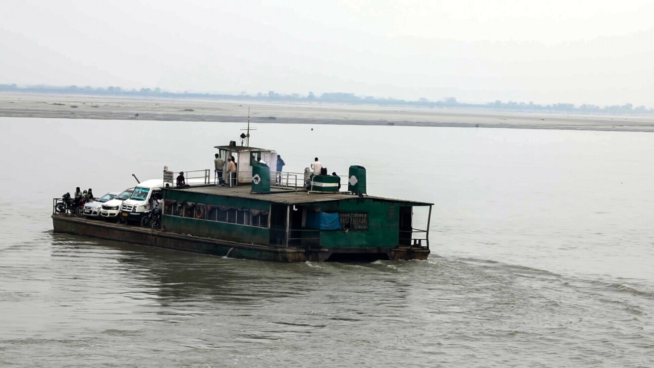 A small ferry boat travels across a body of water. It carries passengers and vehicles.
