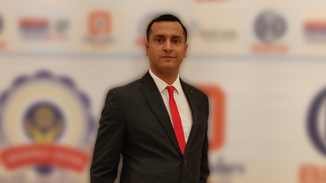 Jayant Jha, the CEO of Yantra stands across a banner in a formal suit