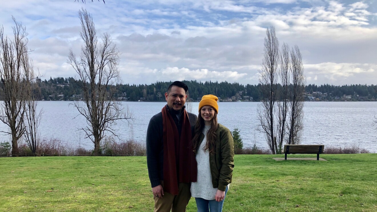A woman and man sit on a bench in front of a lake.