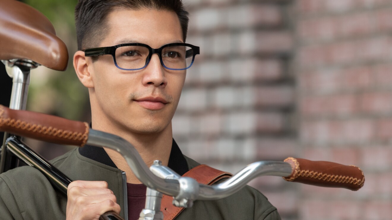 An image of a man wearing his Echo Frames glasses while walking down a sidewalk carrying his bike.